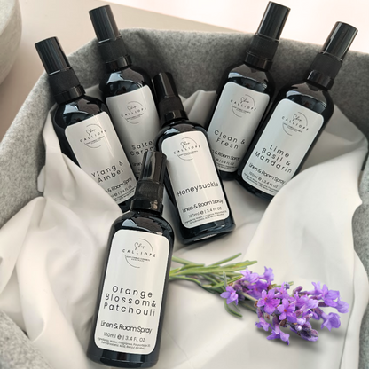A collection of black glass spray bottles with white labels, arranged on a grey surface with a sprig of lavender in the foreground.