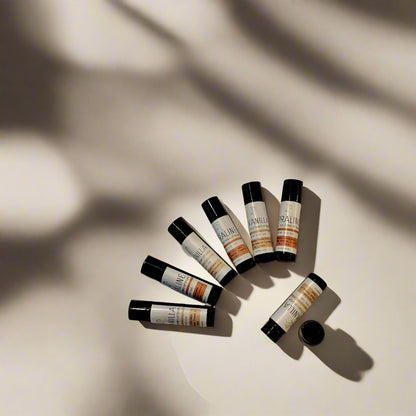 Containers of 'Vanilla & Praline' lip balm with matte black and white labels, positioned on a light background.