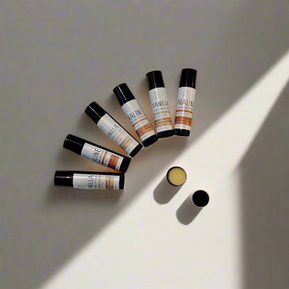 Containers of 'Vanilla & Praline' lip balm with matte black and white labels, positioned on a light background.