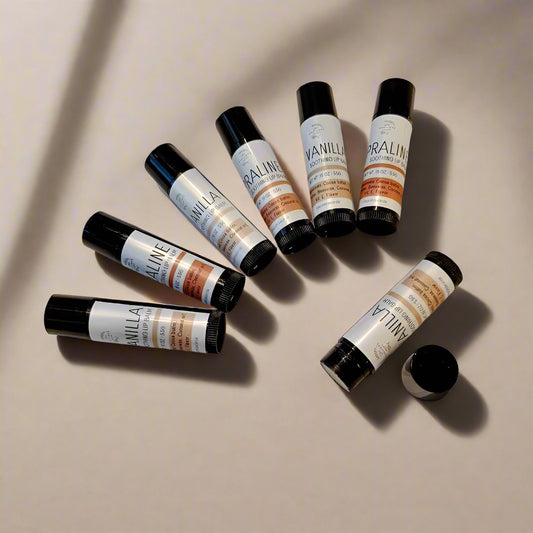  containers of 'Vanilla & Praline' lip balm with matte black and white labels, positioned on a light background.