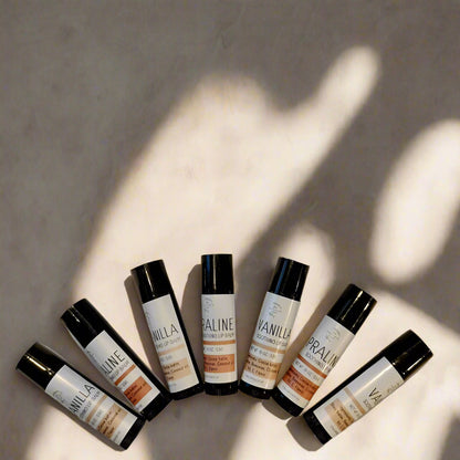 Containers of 'Vanilla & Praline' lip balm with matte black and white labels, positioned on a light background.