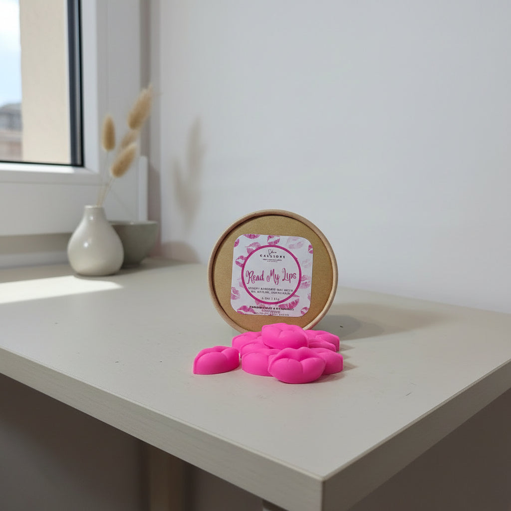 Pink lip-shaped wax melts with a round container labeled 'Read My Lips' on a light surface.