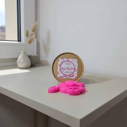 Pink lip-shaped wax melts with a round container labeled 'Read My Lips' on a light surface.