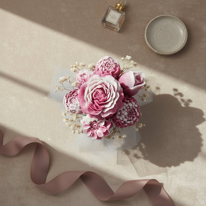 Bouquet of pink flowers with a ribbon on a beige surface, next to a small bottle and dish.