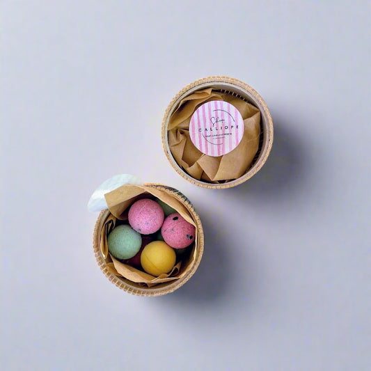 Three colorful bath bombs in a cardboard container on a light gray background