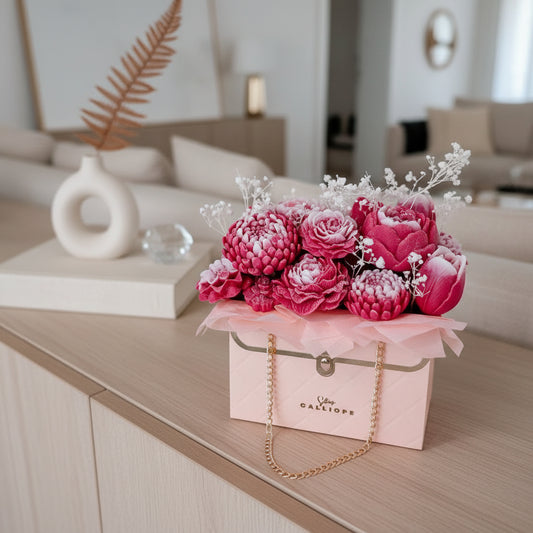 Pink candle floral arrangement in a decorative box on a wooden surface with a blurred living room background.