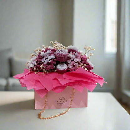 Floral arrangement in a pink box with a gold chain on a white background