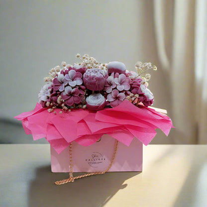Pink floral arrangement in a decorative box with a visible brand name on a light background