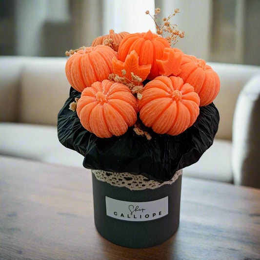 Decorative arrangement of orange pumpkins in a black container with 'Shea Calliope' label on a light background