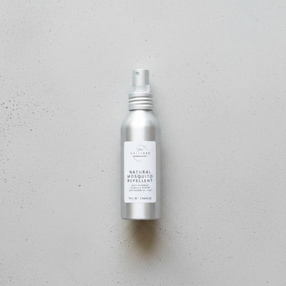 Silver spray bottle labeled 'Natural Mosquito Repellent' on a wooden surface.