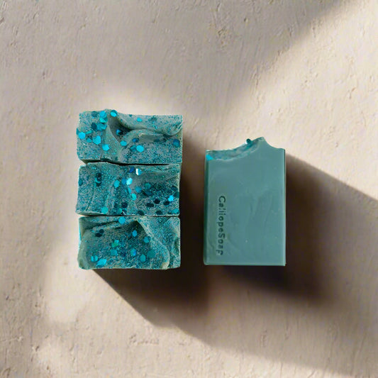 Two pieces of teal soap with glitter on a light beige background