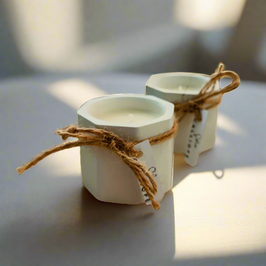 Two hand-painted porcelain candle holders with soy wax candles, tied with twine and tagged with labels.