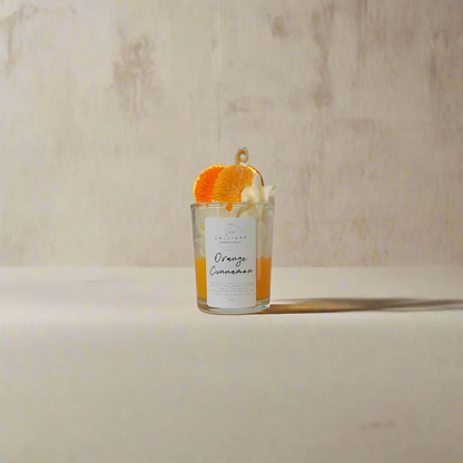 Glass shot candle with orange and cinnamon sticks on a neutral background
