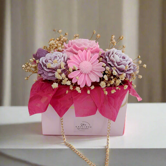 Decorative flower arrangement in a pink box with a gold chain on a neutral background