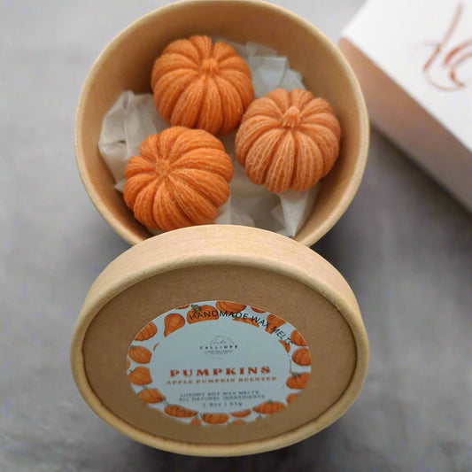 Three orange pumpkins in a cardboard box with a label on a light background