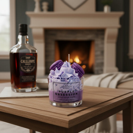 Purple candle labeled 'Purple Obsession' next to a bottle of Calliope brandy on a wooden table with a fireplace in the background.