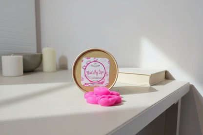 Pink lip-shaped wax melts in front of a round container with a label on a light surface.