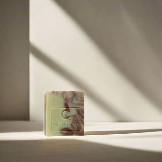 A bar of handcrafted soap with a marbled pattern in shades of beige and white, with a label indicating the brand 'Calliope Soap'.