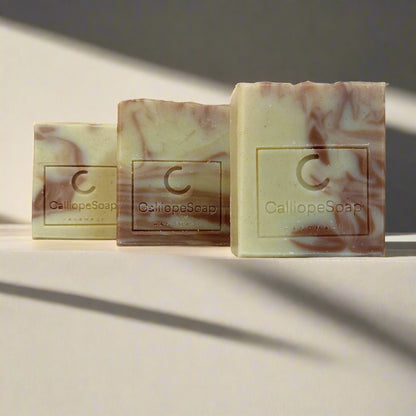 Three bars of handcrafted soap with a marbled pattern in shades of beige and white, each with a label indicating the brand 'Callie Poap'.