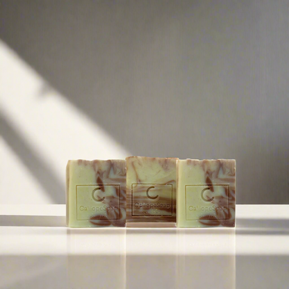Three bars of handcrafted soap with a marbled pattern in shades of beige and white, each with a label indicating the brand 'Calliope Soap'.