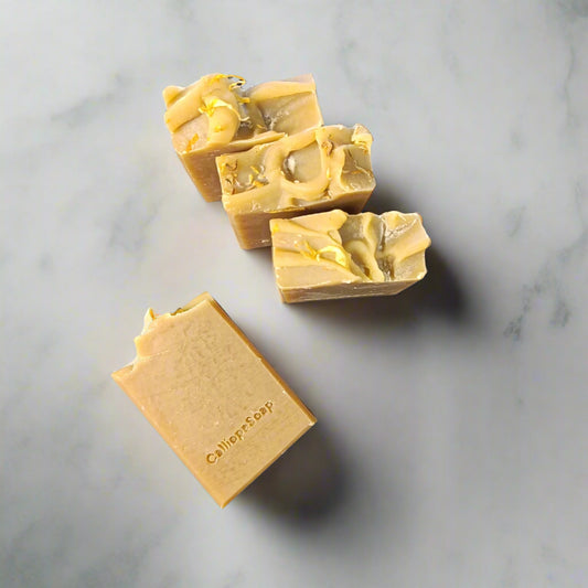 Handmade yellow bar of soap with visible orange and green flecks, placed on a dark wooden surface.