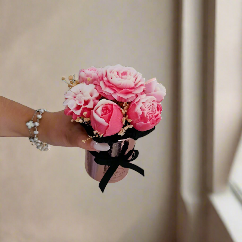 Hand holding a small bouquet of pink flowers with a black ribbon on a white background