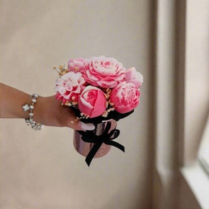 Hand holding a small bouquet of pink flowers with a black ribbon on a white background