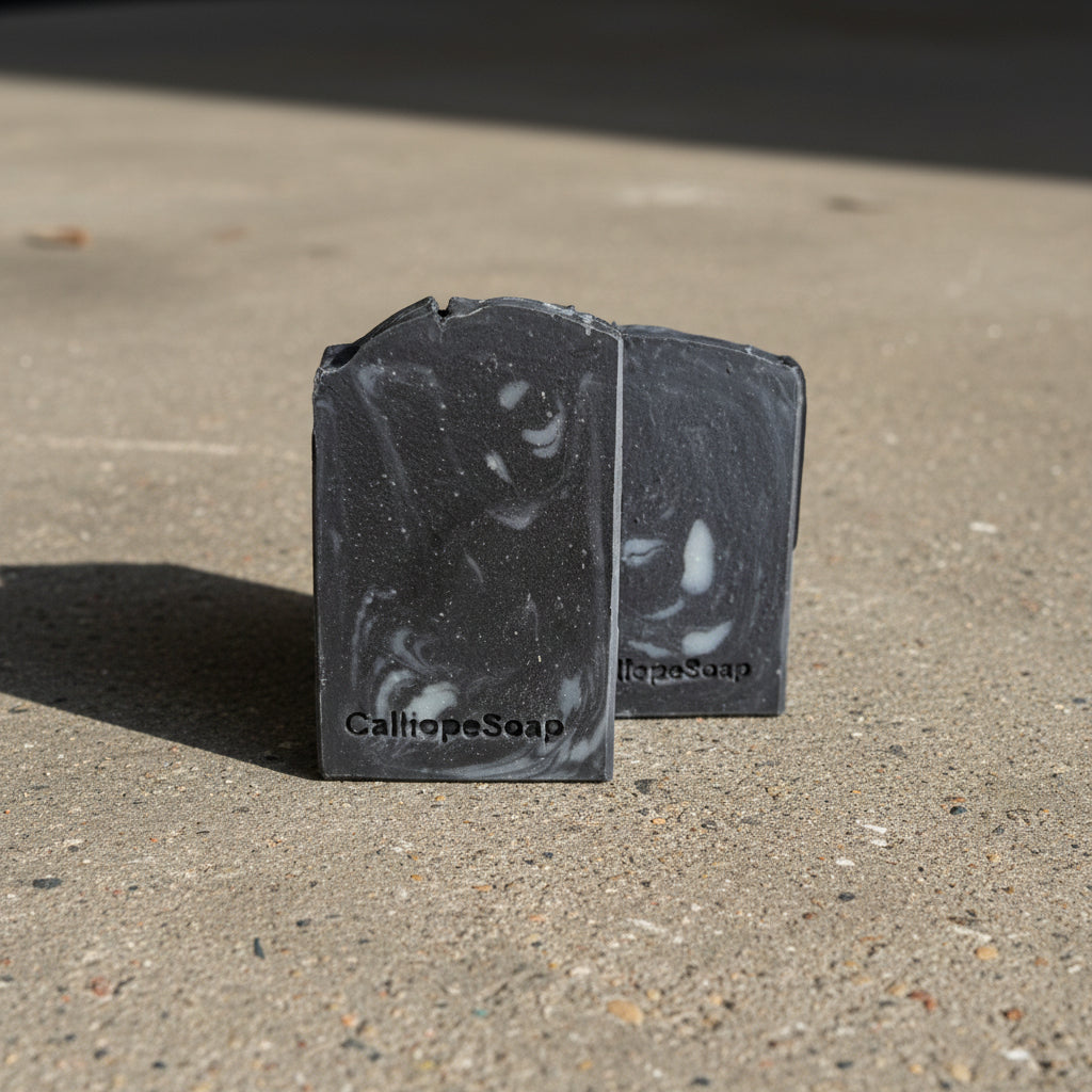 Two black soap bars with visible  CalliopeSoap branding on a light surface.