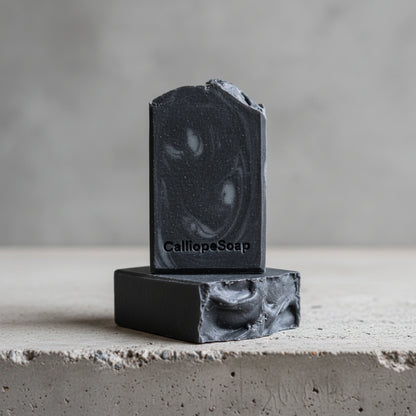 Two blocks of black soap stacked on a light surface with a dark background