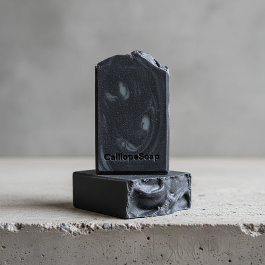 Two blocks of black soap stacked on a light surface with a dark background