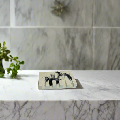 Handcrafted soap dish on a marble surface, minimalistic design, possibly with wooden material, accompanied by a bottle of liquid.