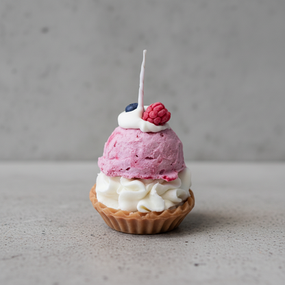 Ice cream tart candle with pink ice cream, whipped cream, and a raspberry on a gray background