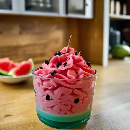 Pink candle in a glass with watermelon theme on a wooden table.