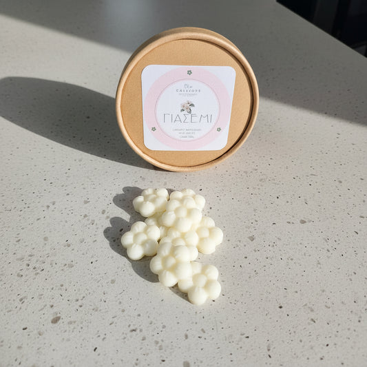 Χειροποίητα wax melts γιασεμί σε σχήμα λευκών λουλουδιών δίπλα στη χάρτινη οικολογική συσκευασία Calliope.
