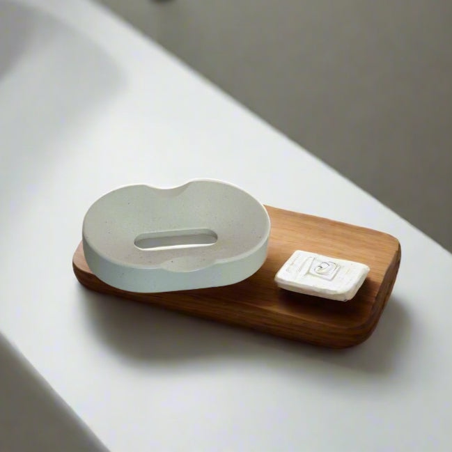 Handcrafted soap dish on a marble surface, minimalistic design, possibly with wooden material, accompanied by a bottle of liquid.
