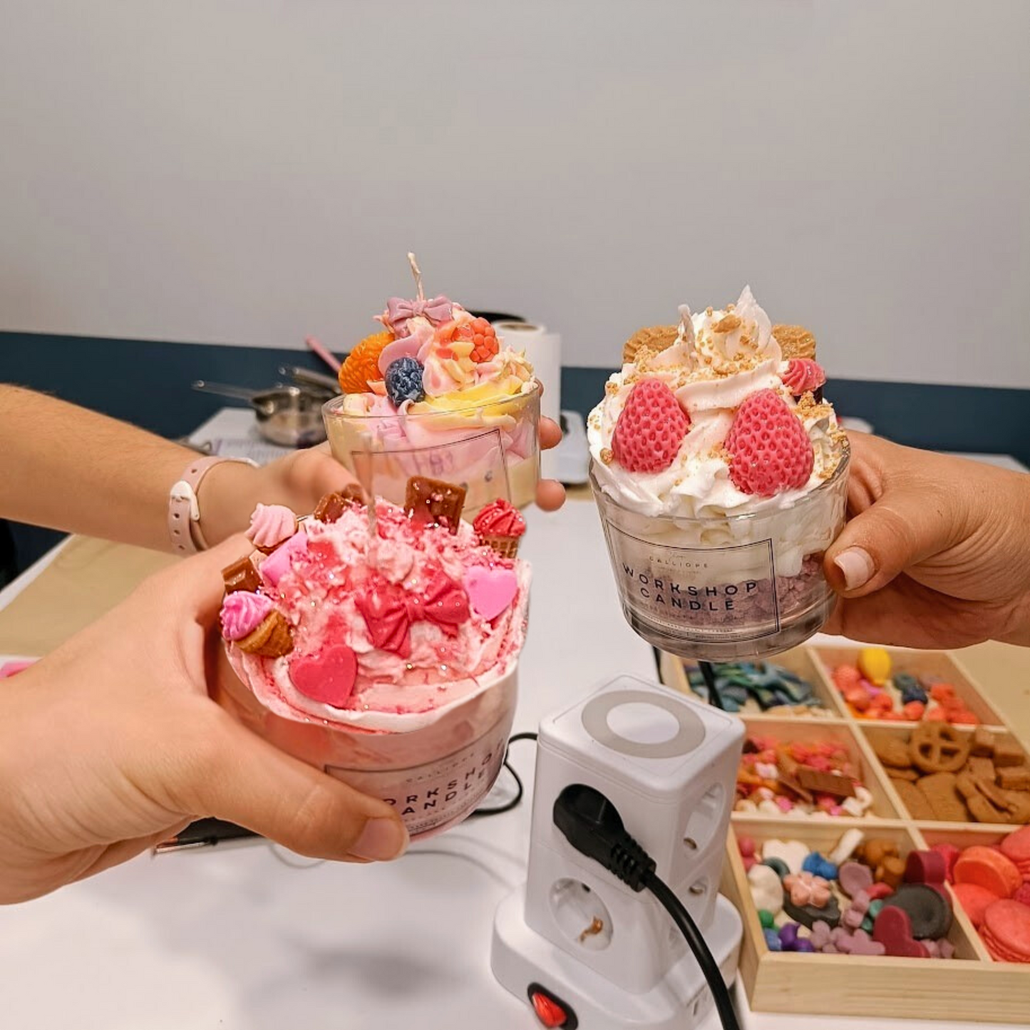 Two hands holding decorated candles with a small white appliance on a table.