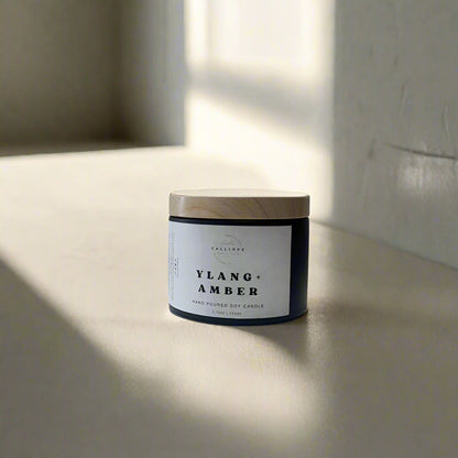 Candle jar labeled 'Ylang Amber' on a white surface with a light gray background